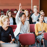 Conference participants seated with a woman raising her hand